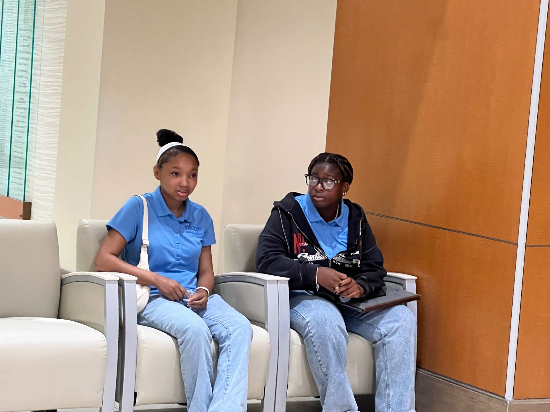 Two Summer Institute students in Village Public Health polos waiting in a hospital lobby