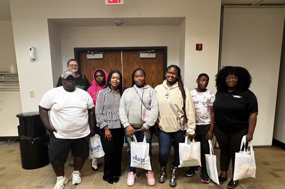 A multigenerational group of youth and trusted adults holding Village Public Health tote bags after a community session.